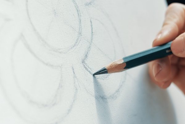 Una mano dibujando con un lápiz negro sobre un papel de color blanco